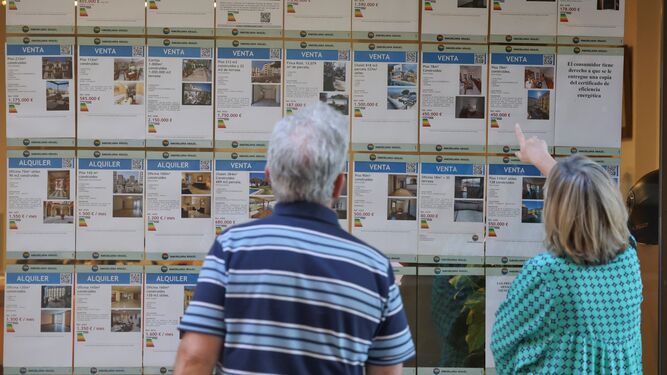 Dos personas revisan las ofertas expuestas en el escaparate de una inmobiliaria de Málaga.